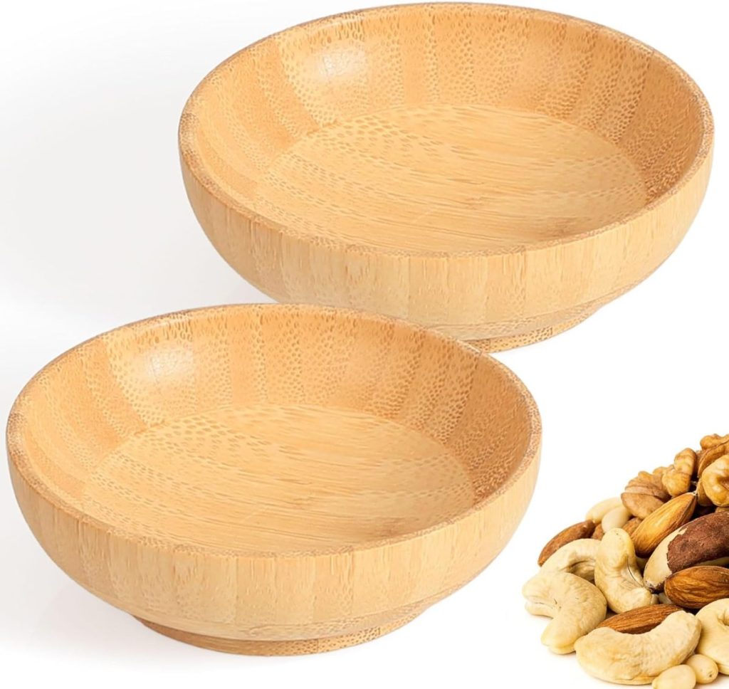 Two empty round bamboo bowls are placed side by side, with a small pile of mixed nuts, including cashews and walnuts, in the corner. Behind them, delicate floral pots add a soft touch to the arrangement.