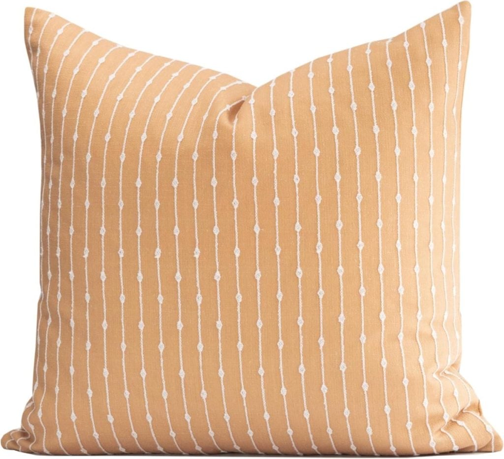 Square throw pillow with a light orange cover featuring vertical white dotted lines and small geometric shapes.