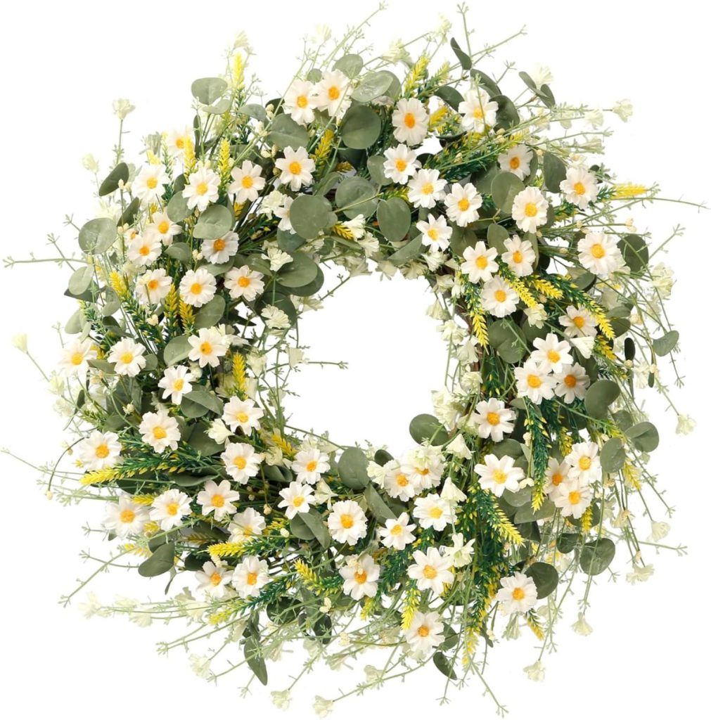 A circular window wreath adorned with small white daisy-like flowers, green leaves, and yellow accents, arranged in a dense, natural style.