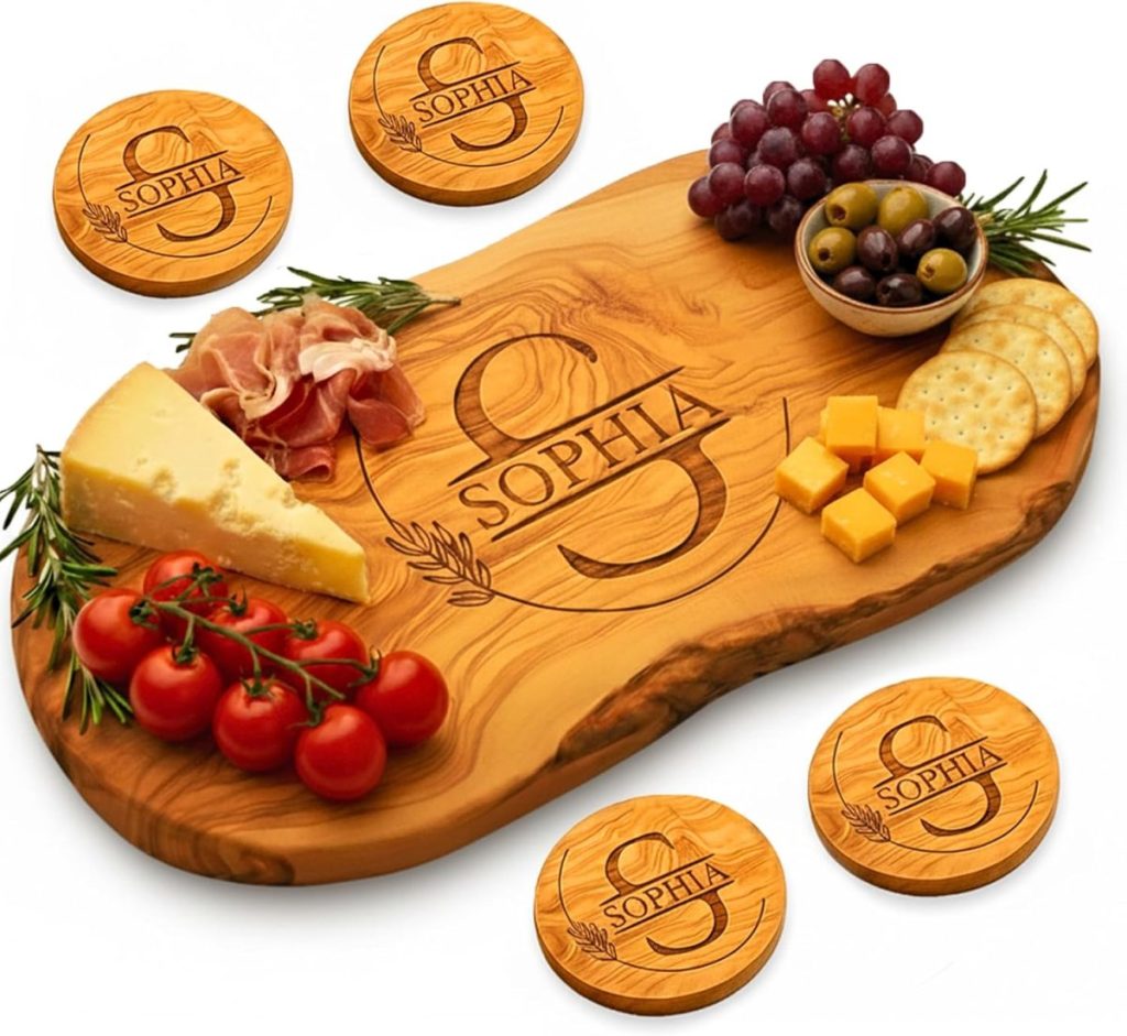 A wooden charcuterie board engraved with "Sophia" holds cheese, grapes, olives, crackers, tomatoes, and cured meat. Matching engraved coasters surround the board.