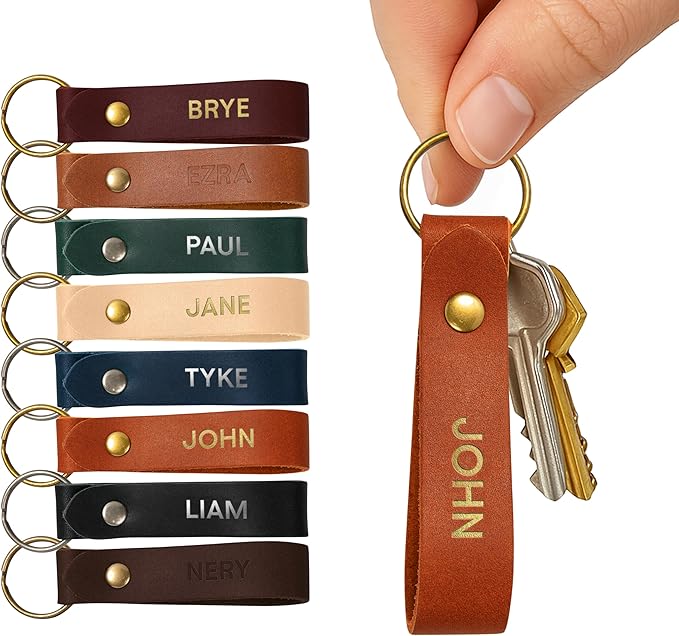 Eight leather keychains in various colors, each labeled with a different name, are displayed next to a hand holding a brown "JOHN" keychain with two keys attached.