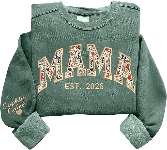 A green sweatshirt with "MAMA EST. 2026" printed on the front in floral block letters and "Sophia Caleb" embroidered on the sleeve with a small heart.