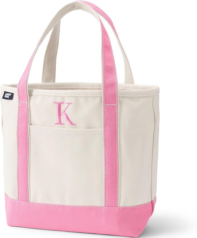 A beige canvas tote bag with pink handles and trim, featuring a front pocket and the letter &ldquo;K&rdquo; embroidered on the front.