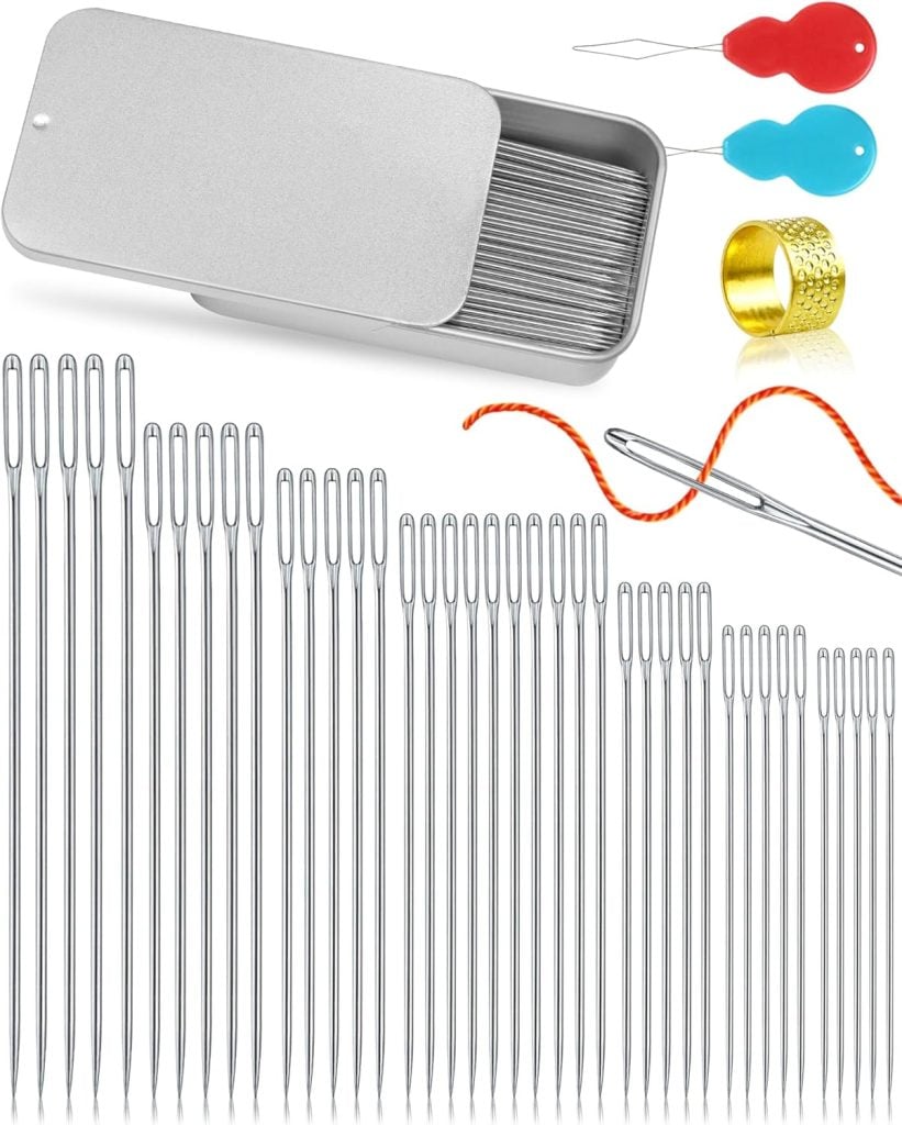A sewing kit with metal needles in various sizes, a metal storage case, two needle threaders, a thimble, and an orange thread through one needle.