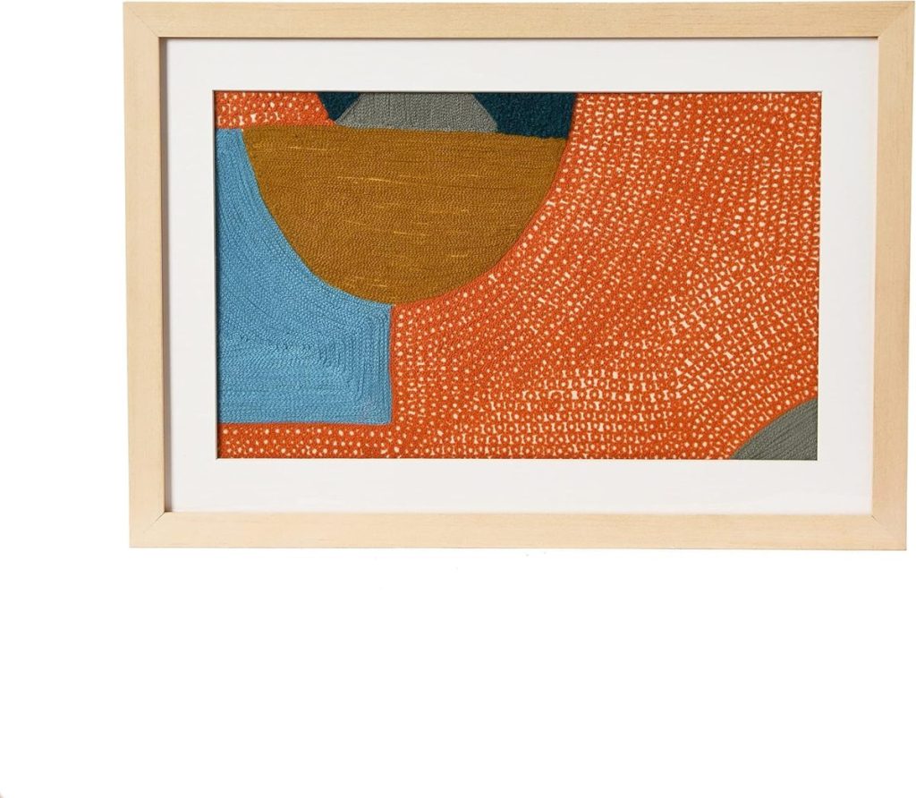 Framed abstract artwork featuring textured shapes in orange, blue, mustard yellow, and gray with a white mat and light wood frame.