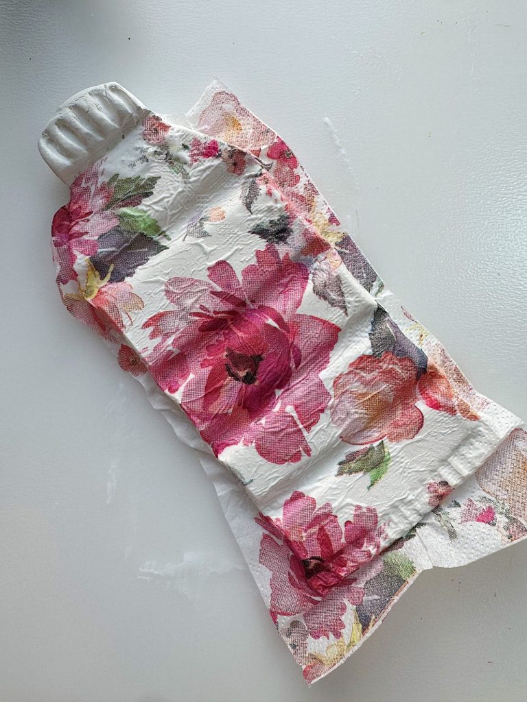 A floral-patterned paper napkin is molded around a plastic bottle, lying on a white surface.