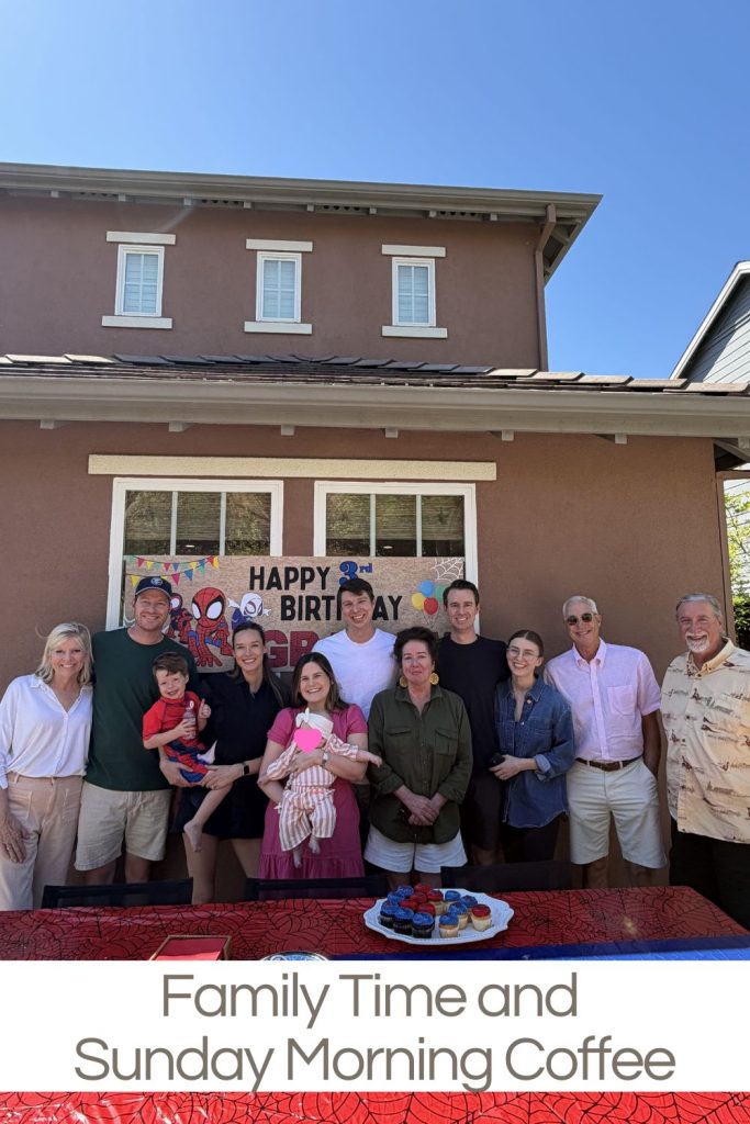 A group of twelve people poses in front of a house with a &ldquo;Happy Birthday&rdquo; banner and a table with coffee and pastries in the foreground.