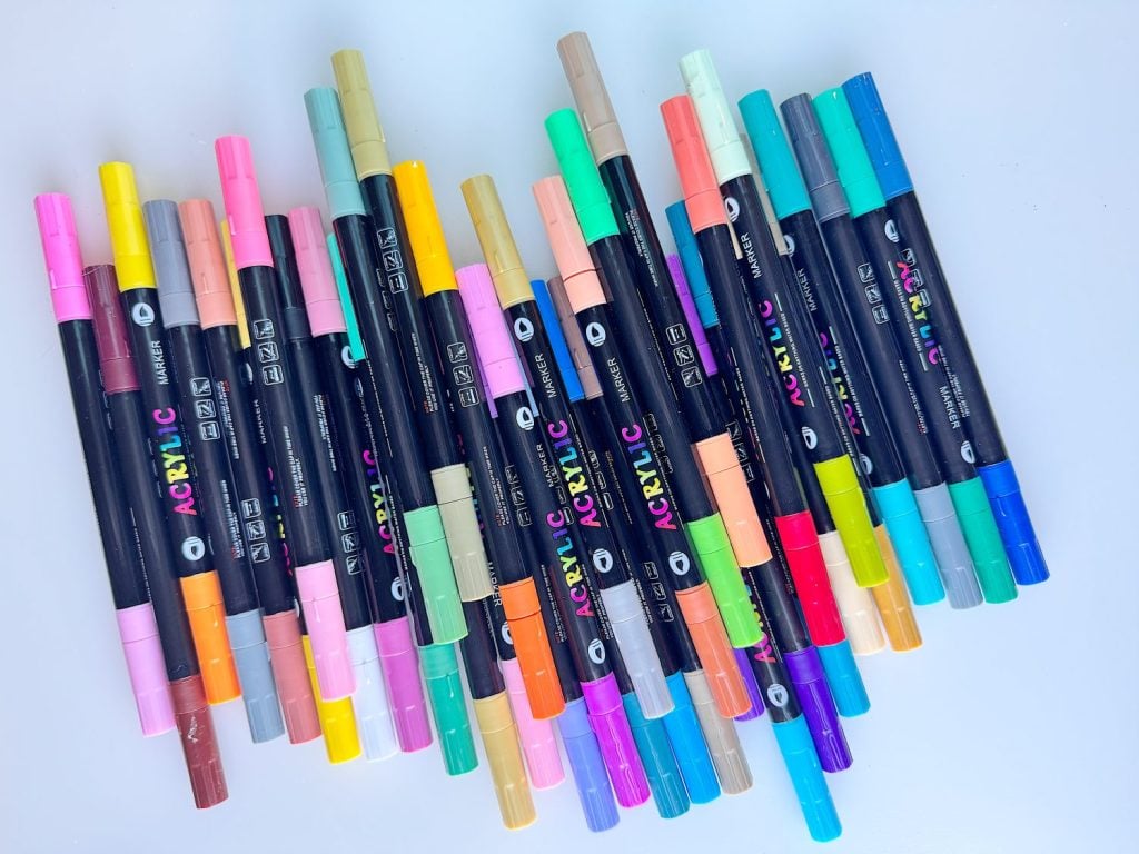 A variety of dual-tip acrylic paint markers arranged in a slightly fanned pattern on a white surface.