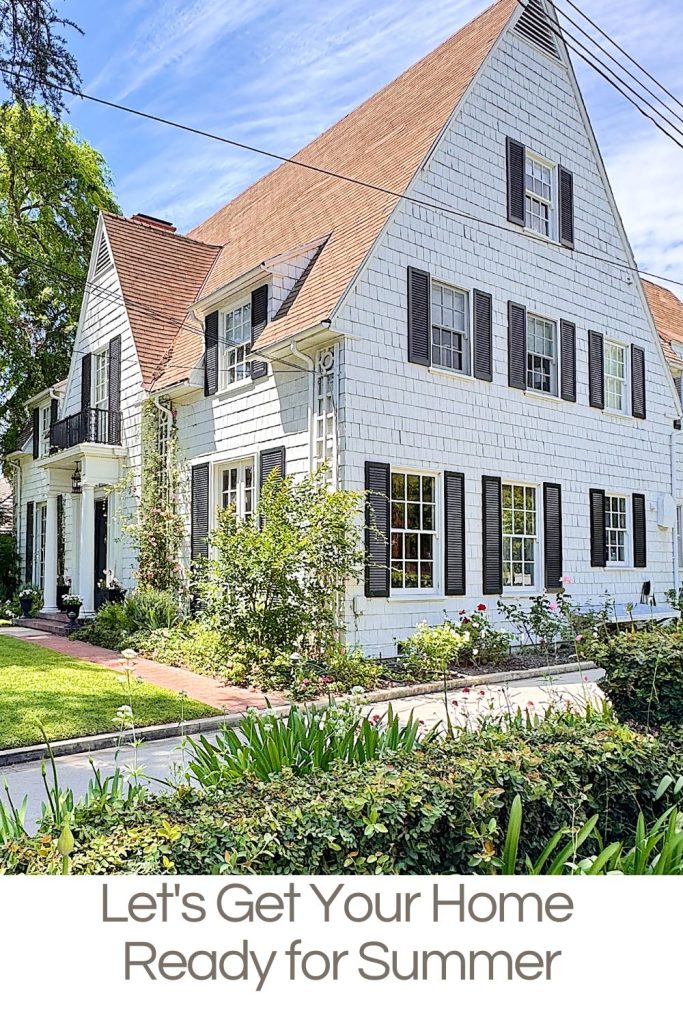 A large white house with brown roof and black shutters surrounded by greenery under a blue sky, with the text &ldquo;Let&rsquo;s Get Your Home Ready for Summer&rdquo; at the bottom.