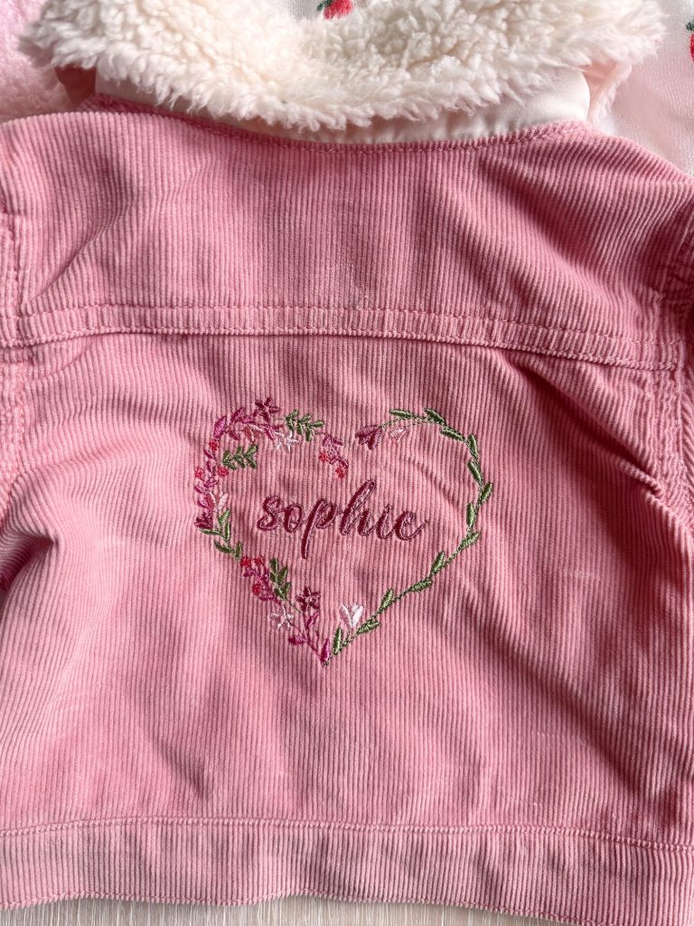 Pink corduroy jacket with a fuzzy collar, featuring &ldquo;sophie&rdquo; embroidered inside a heart-shaped floral wreath on the back.