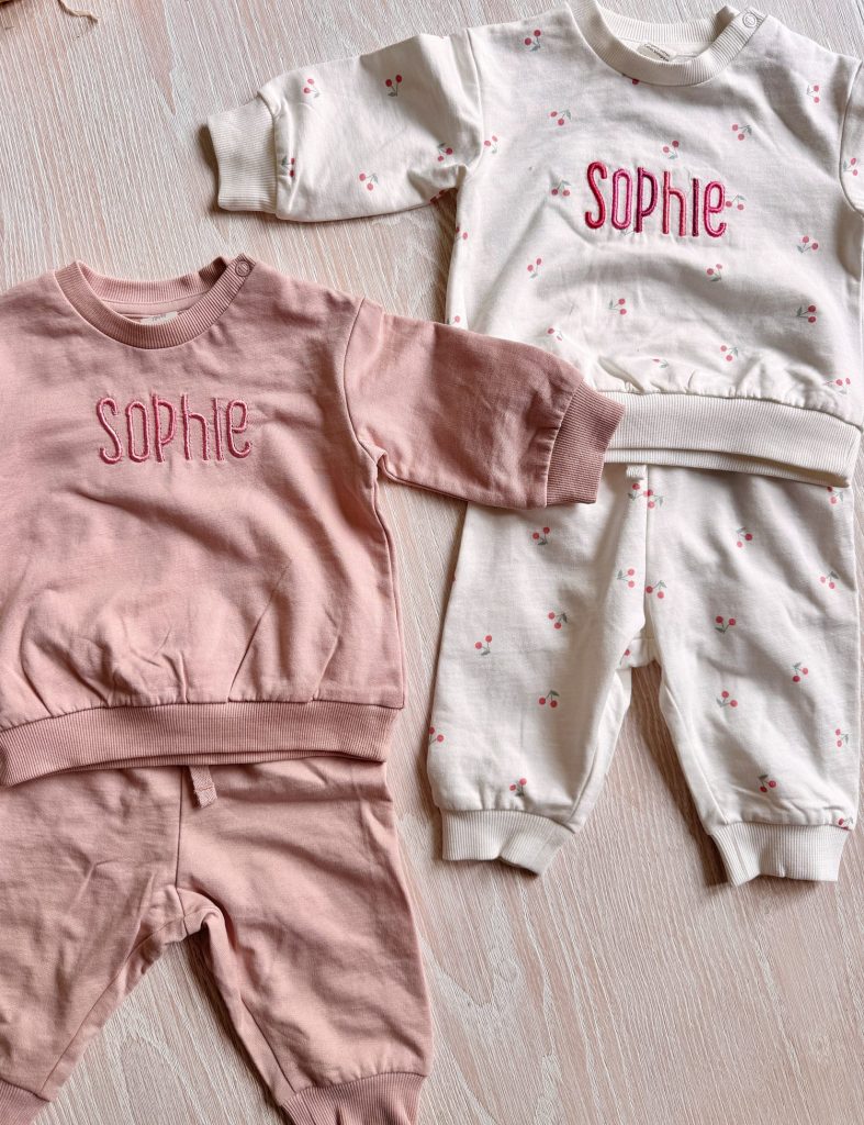 Two sets of children's clothes, one pink and one white with small floral patterns, both featuring the name "Sophie" embroidered on the tops.