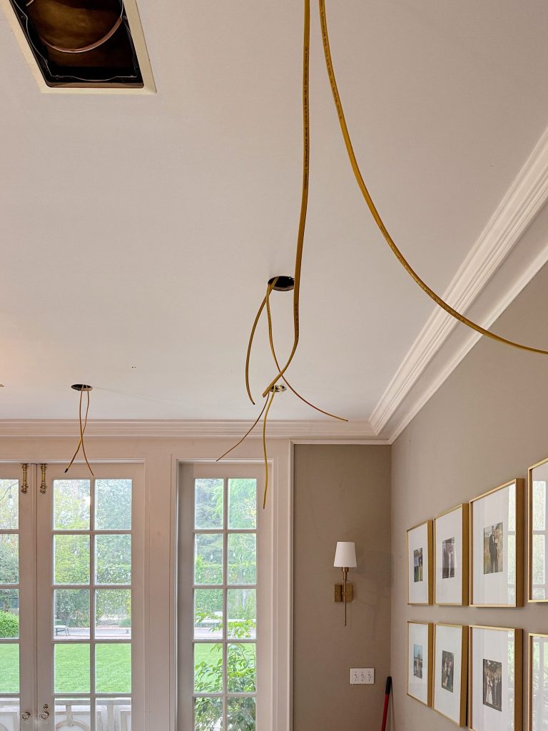 Ceiling with exposed yellow electrical wires hanging down, indicating ongoing light fixture installation in a room with framed photos and French doors.