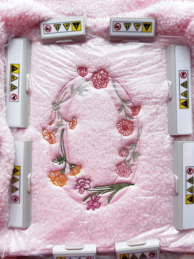A pink fabric with embroidered flowers is surrounded by eight white plastic devices featuring yellow and red warning labels.