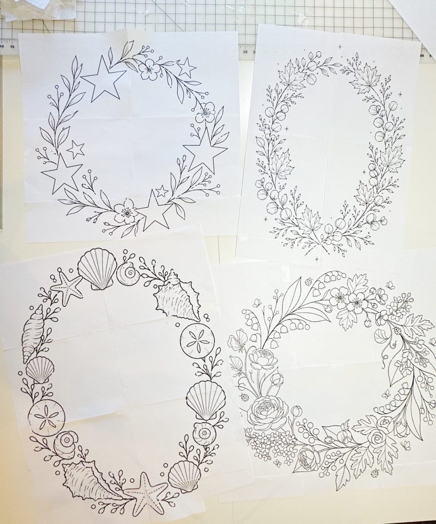 Four sheets of paper display hand-drawn circular wreath designs featuring stars, flowers, seashells, and berries, placed on a white surface.