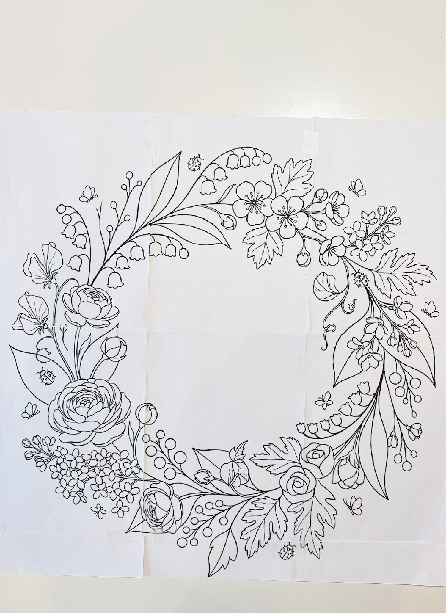 Black and white line drawing of a circular floral wreath with various flowers, leaves, and small berries on a white background.