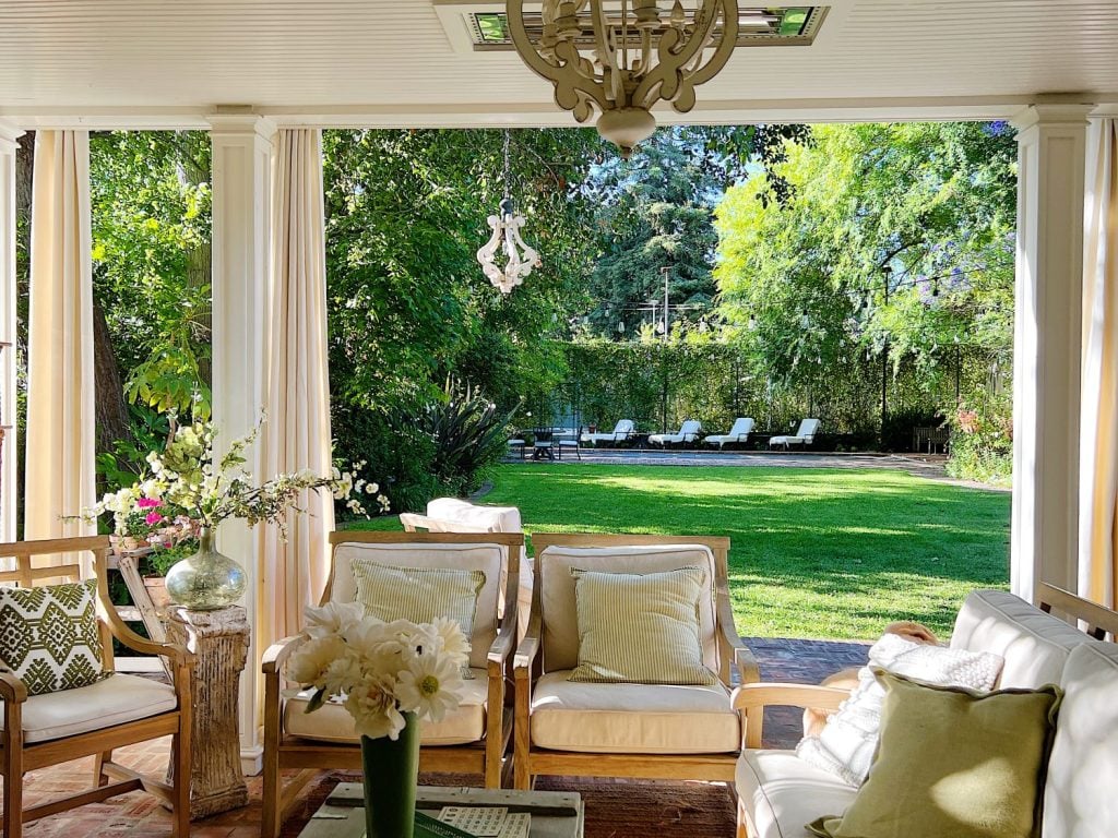 Sunny outdoor patio with cushioned chairs and a coffee table, overlooking a green lawn with lounge chairs and trees in the background.