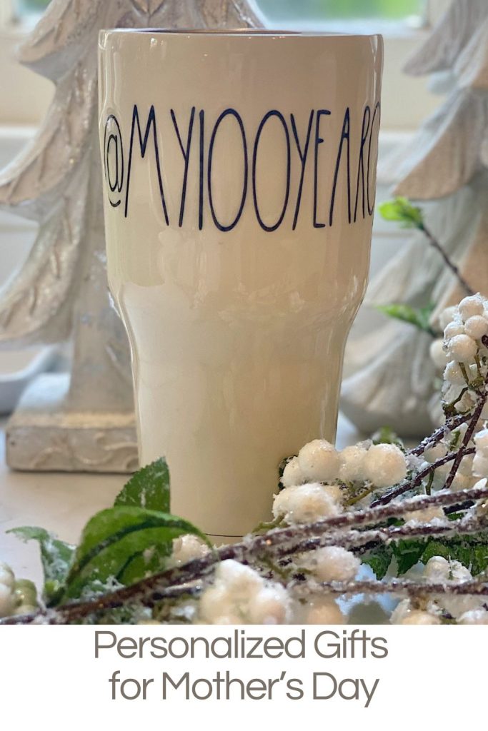 A white ceramic cup with the text "@MY100YEARS" sits on a table next to decorative white berries and green leaves. Text below reads: "Personalized Gifts for Mother's Day.