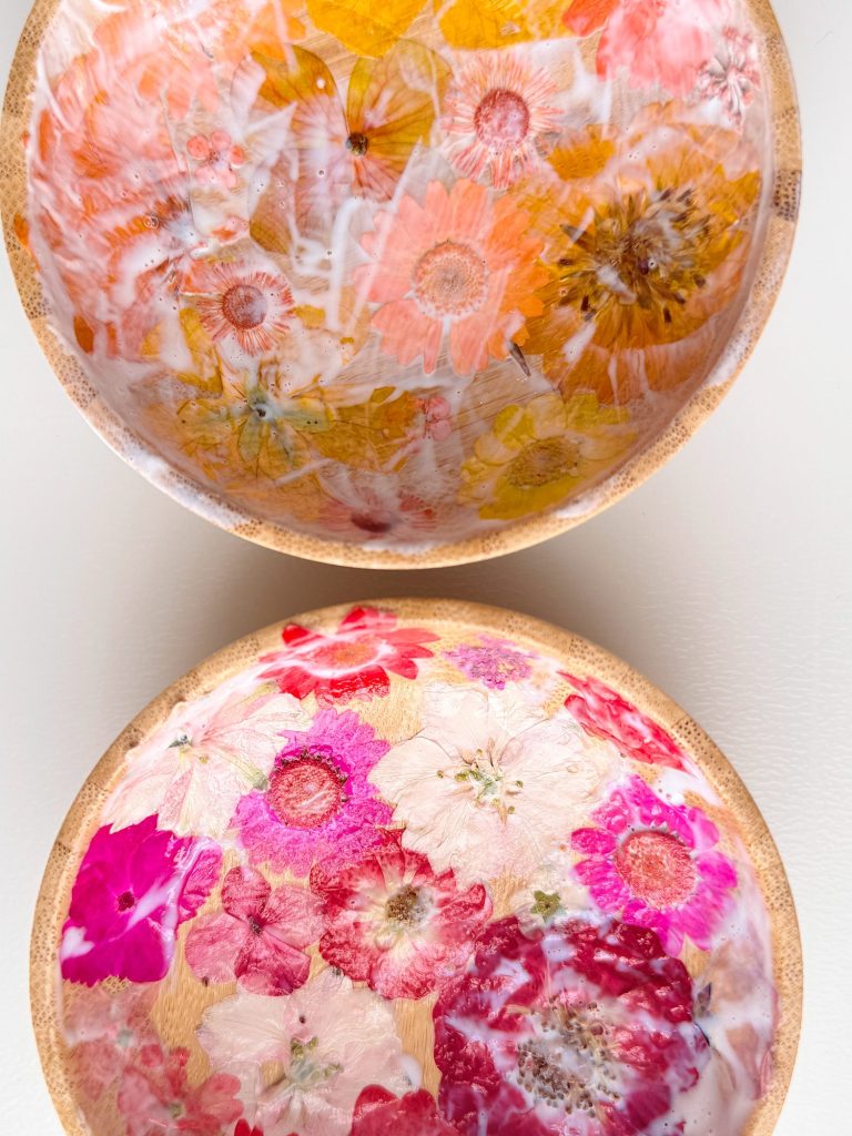 Two round wooden bowls with glossy interiors decorated with pressed, colorful flowers in shades of pink, red, yellow, and white.