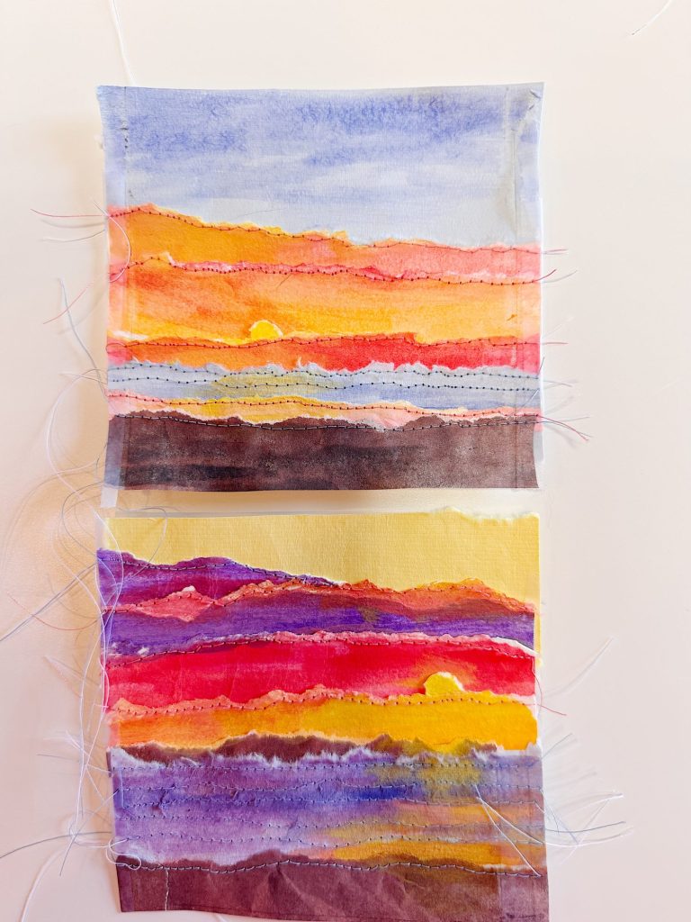Two rectangular fabric swatches feature layered, colorful painted sunset designs with visible stitching and frayed threads on a light background.