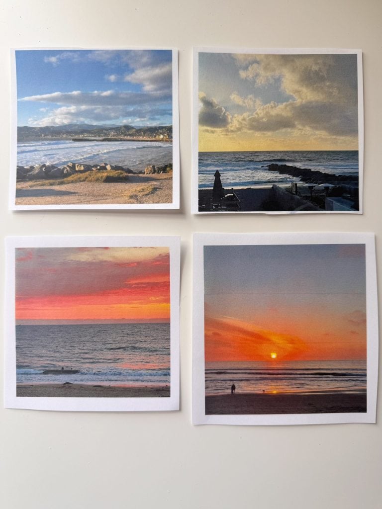 Four printed photographs of ocean sunsets and sunrises are displayed on a white surface, each showing different sky colors and coastal scenes.