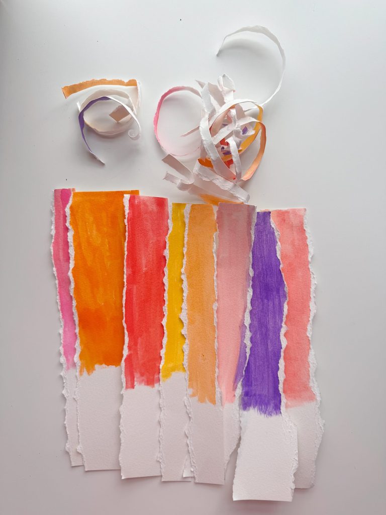 Torn strips of paper painted in orange, red, pink, peach, and purple are arranged vertically on a white surface, with curled strips at the top.
