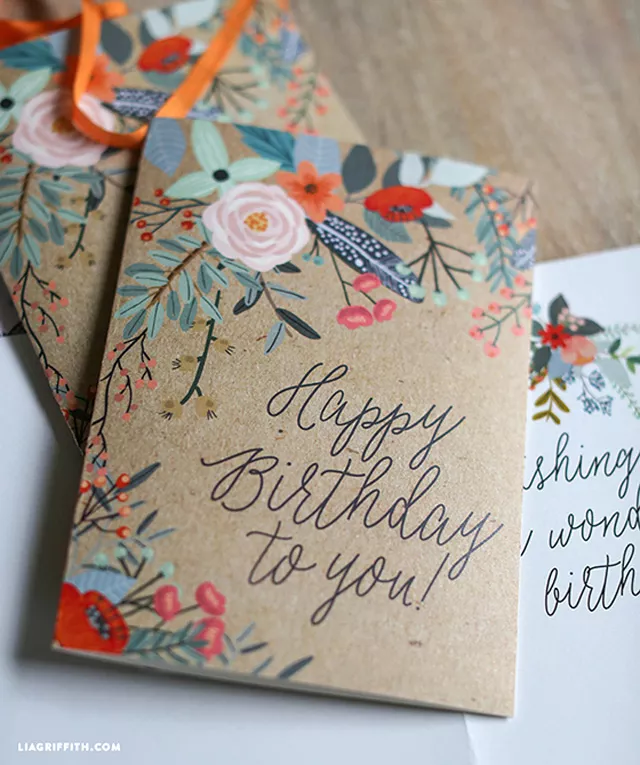 A floral-themed birthday card with "Happy Birthday to you!" written on the front, lying on top of a matching gift bag and an open card with a partial message visible.