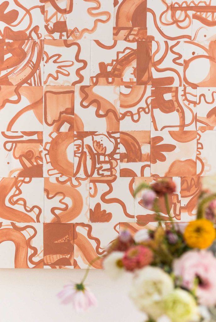 Abstract artwork with terracotta-toned geometric and organic shapes on a white background; blurred bouquet of flowers in the foreground.