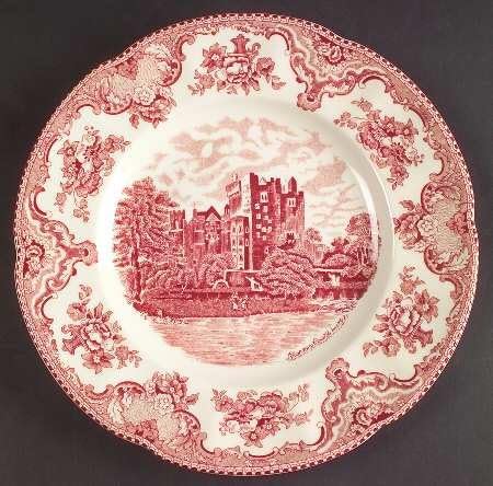 Decorative ceramic plate with a red and white pattern, featuring a castle scene in the center and ornate floral designs around the rim&mdash;a charming piece Theo of Golden Book Club would admire.