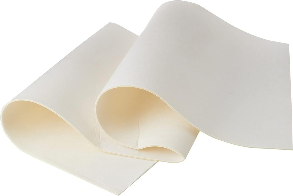 Two large sheets of plain, off-white paper are partially rolled and overlapping on a flat surface.