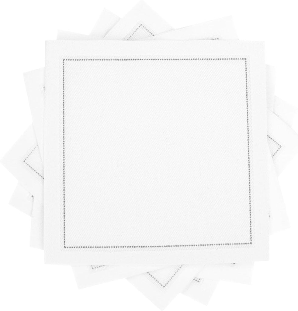 Stack of white embroidered cocktail napkins featuring a subtle stitched border, neatly arranged with corners overlapping on a plain background.