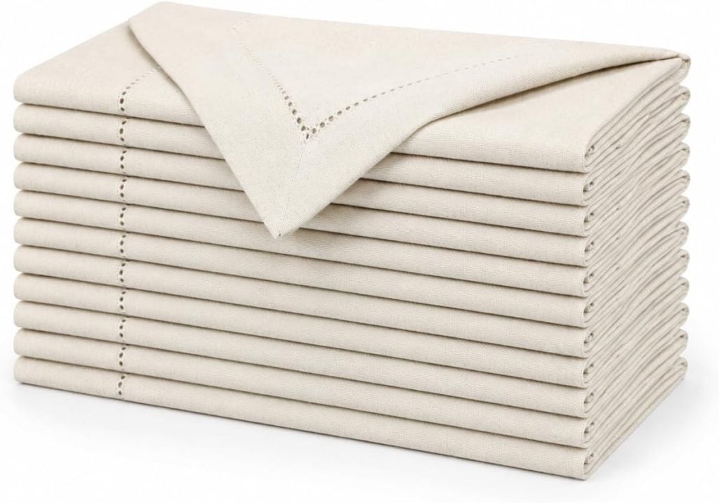 A neatly stacked pile of folded beige cloth napkins with decorative stitching on the edges.