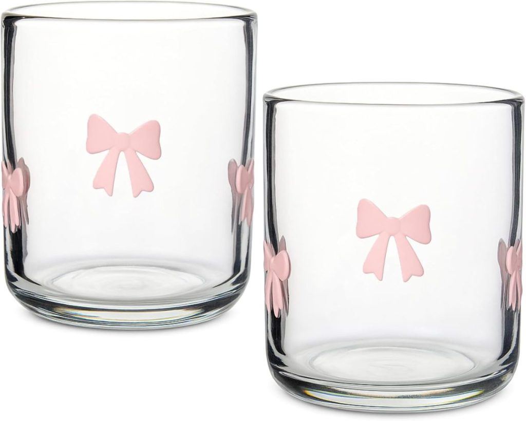 Two clear glass tumblers decorated with light pink bow designs on the sides, perfect for pairing with embroidered cocktail napkins at your next gathering.
