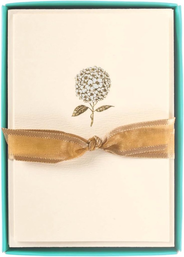 A cream-colored card with a gold hydrangea design and elegant wax seals, tied with a gold ribbon, placed in a turquoise box.