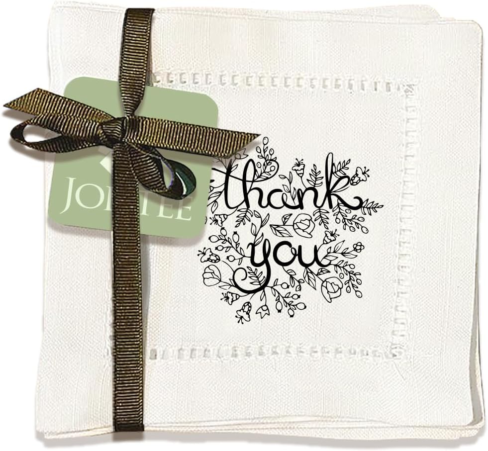 A white embroidered cocktail napkin with "thank you" and floral designs in black, tied with a brown ribbon and a green tag.