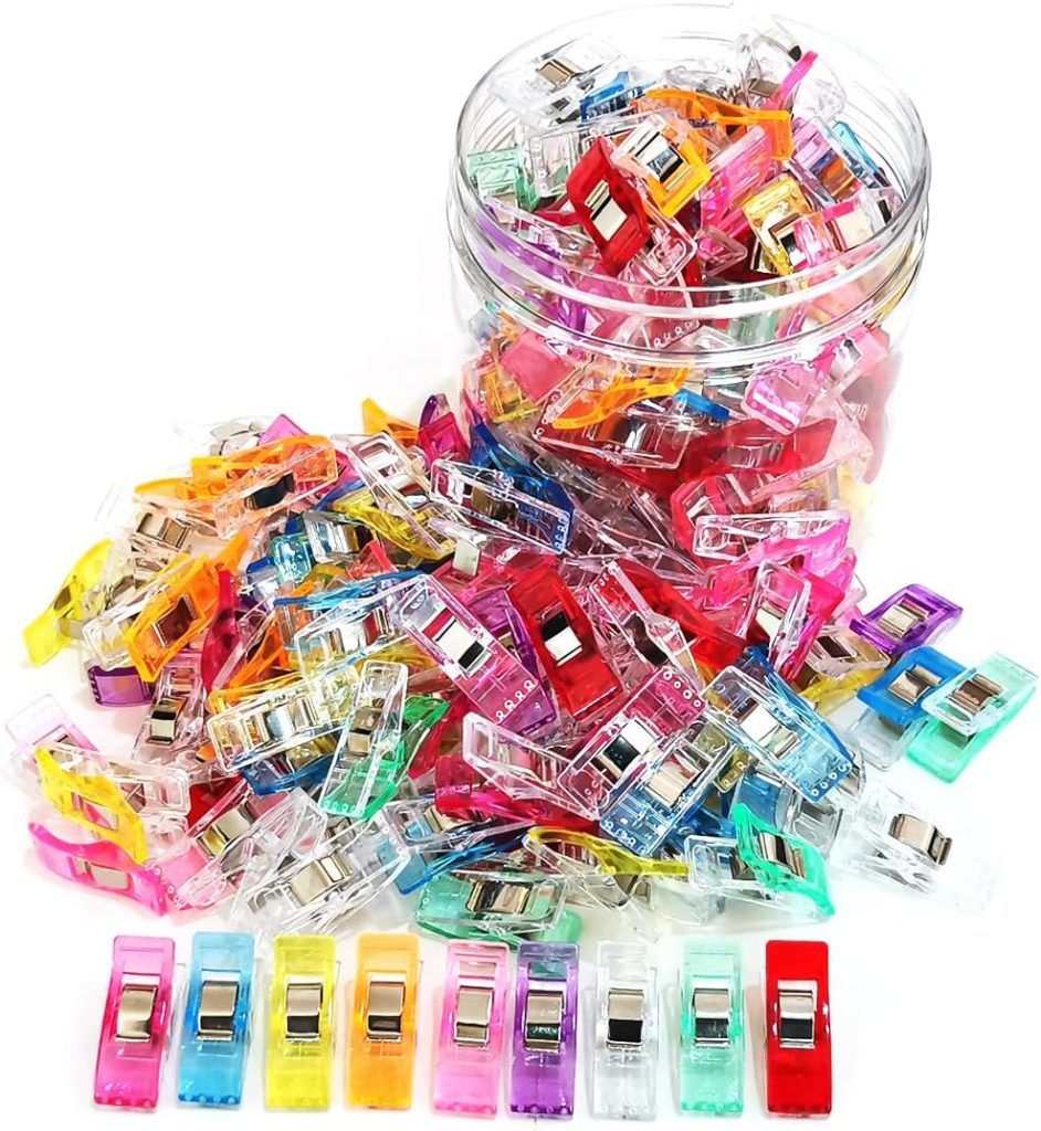 A clear plastic jar tipped over, spilling out numerous colorful fabric clips in various colors, with eight clips neatly lined up in front.