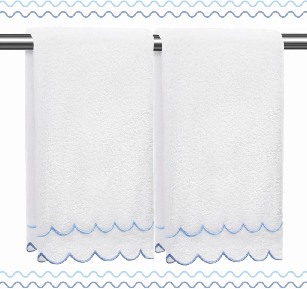 Two white towels with blue scalloped edges hang side by side on a metal towel bar, with a wavy blue border in the background.