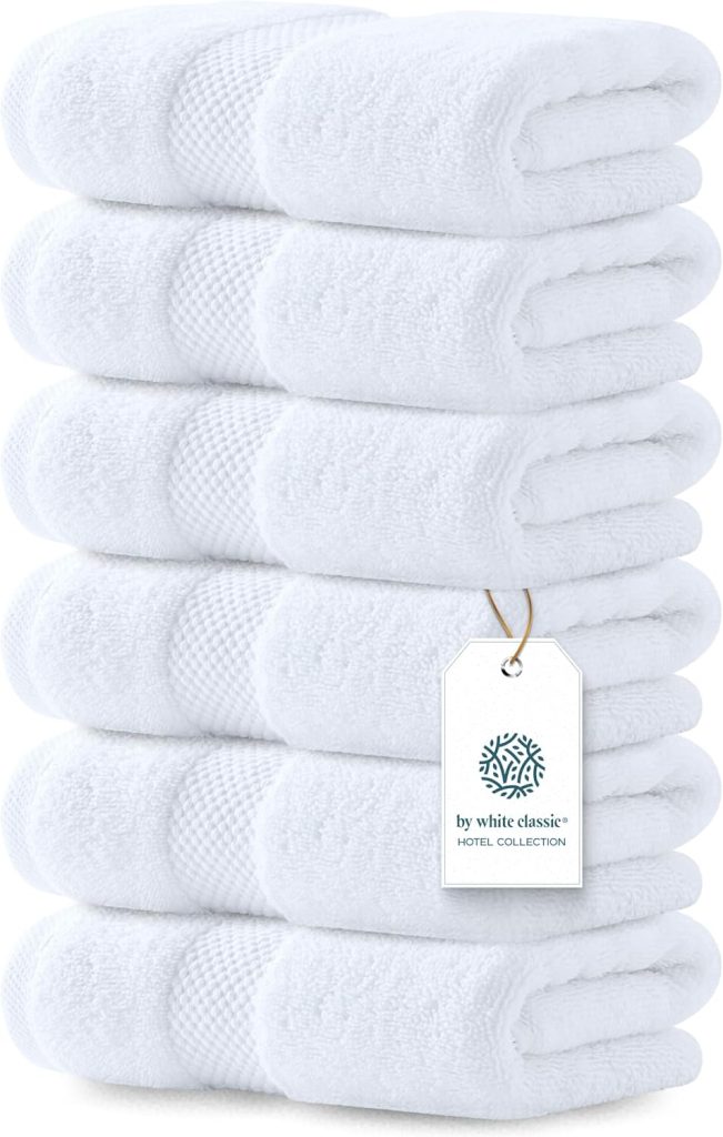 A stack of six folded white towels with a hanging tag labeled "by white classic HOTEL COLLECTION.