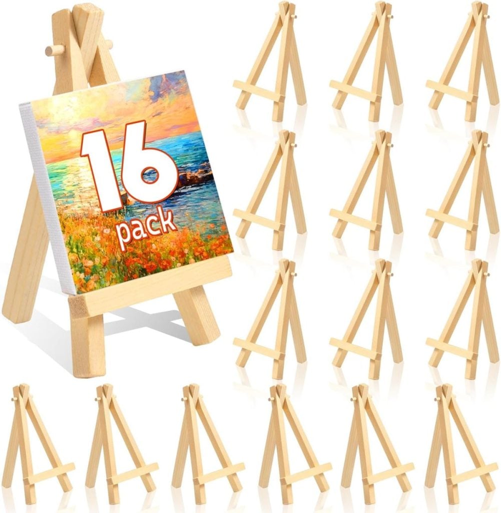 Sixteen small wooden easels are displayed, with one holding a colorful painting and the text "16 pack"—perfect for Memorial Day crafts. The remaining easels are empty and arranged in neat rows.
