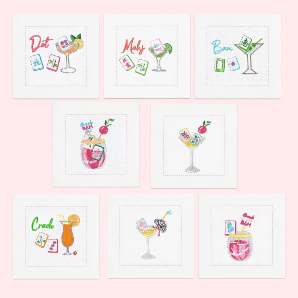 Seven Embroidered Cocktail Napkins with white fabric feature playful designs of cocktails and Mahjong tiles, arranged in two neat rows on a light pink background.