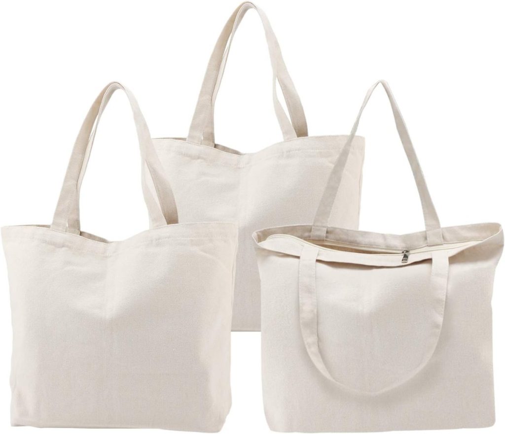 Three plain, off-white canvas tote bags with handles, two standing upright and one lying flat, displayed against a white background.