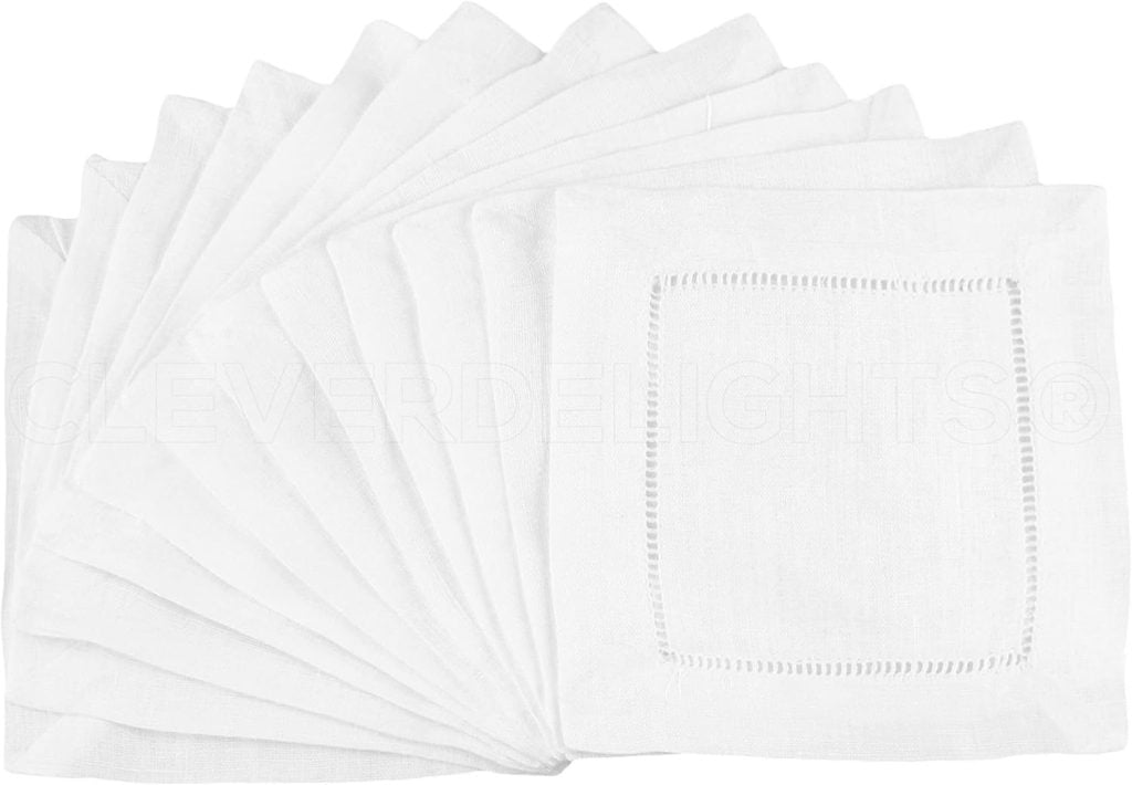 A set of white, folded embroidered cocktail napkins with a simple square hemstitch border design, fanned out in a semi-circle.