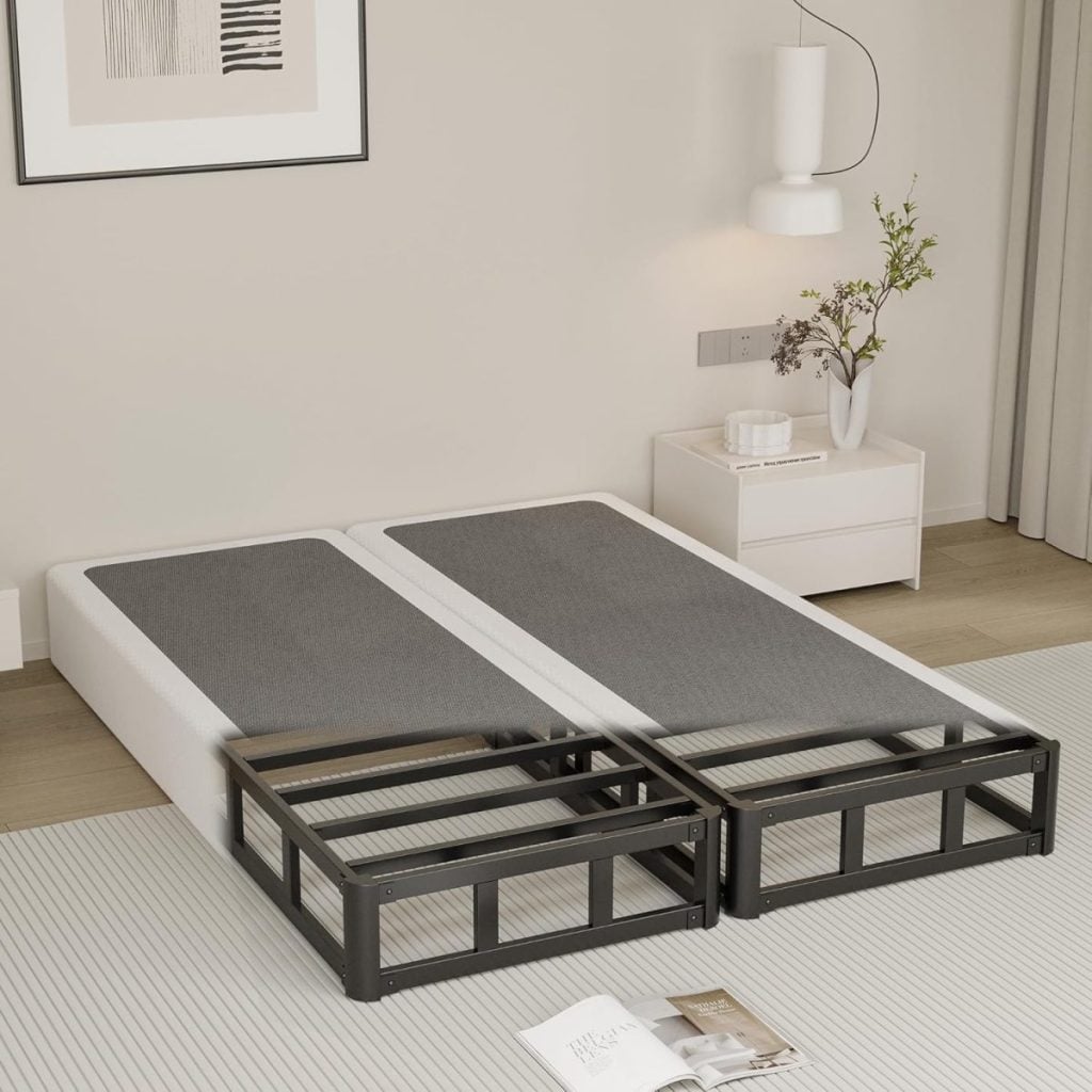 Two twin adjustable bed bases with gray mattresses are placed side by side in a modern bedroom with minimal decor and a nightstand holding a vase and books.