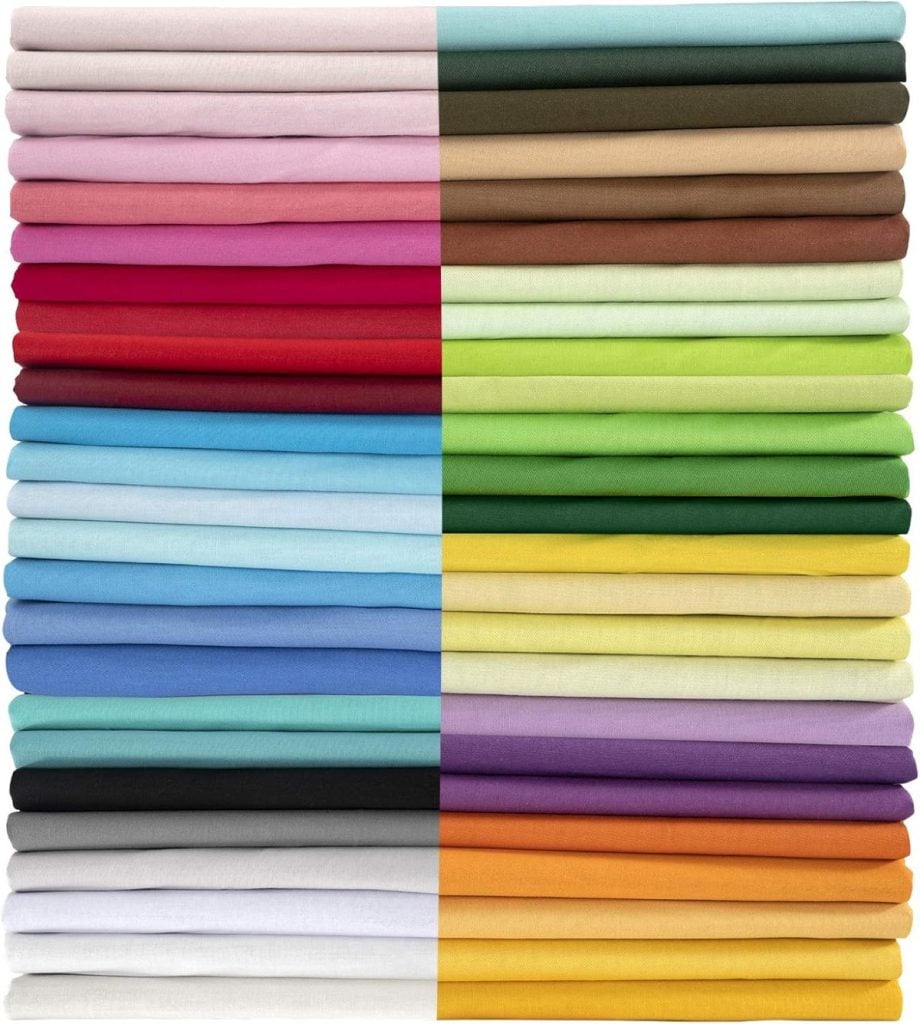 Stacks of folded embroidered cocktail napkins in a variety of solid colors, arranged in two columns with shades ranging from light pastels to bold and dark hues.