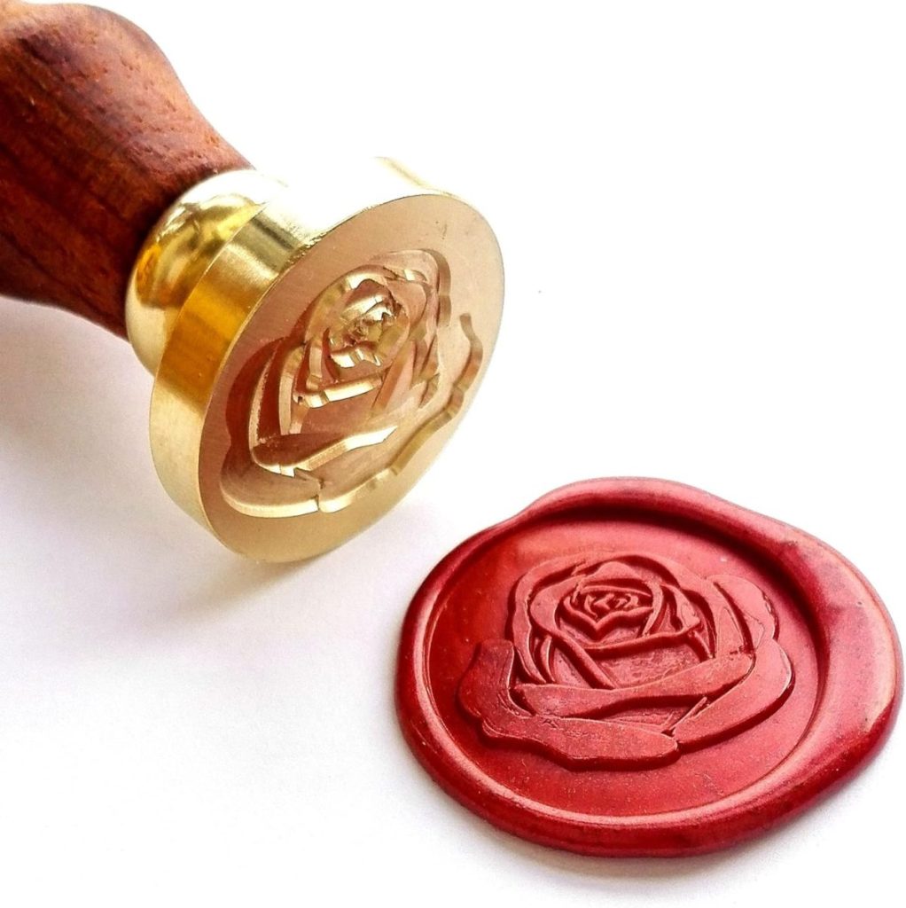A brass wax seal stamp with a rose design sits next to a red wax seals impression of the same rose on a white background.