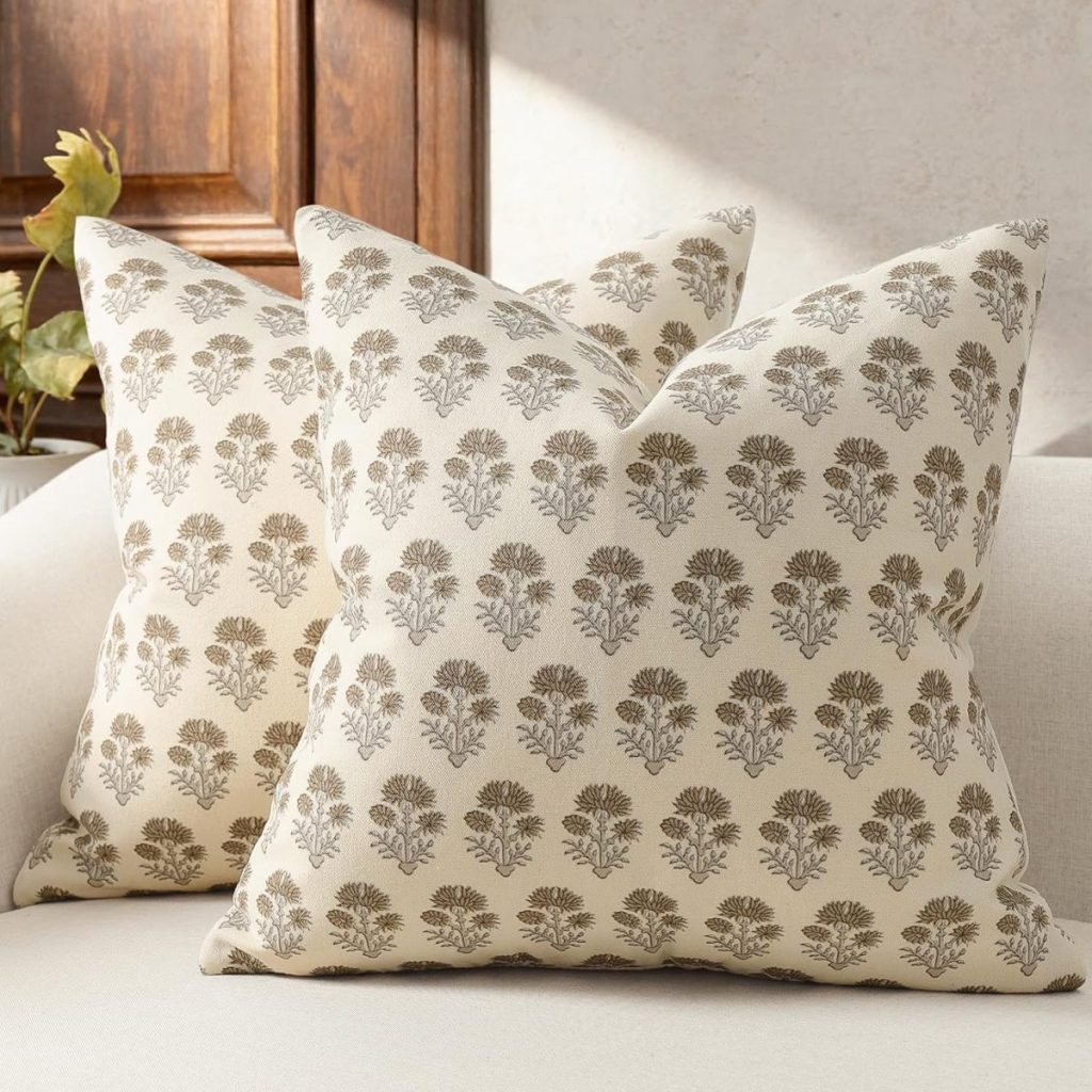 Two beige throw pillows with brown floral patterns, perfect for summer crafting inspiration, are placed on a light-colored sofa in a sunlit room.
