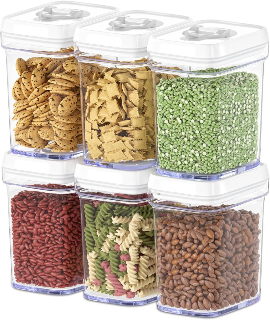 Six clear plastic containers with white lids, each holding different dry foods including cookies, pasta, green peas, red rice, spiral pasta, and brown grains.