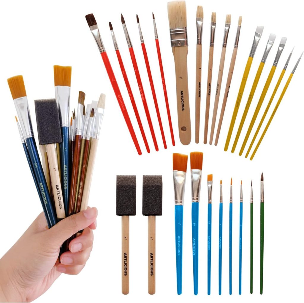 A hand holds various paintbrushes and foam brushes, with more brushes arranged in groups on a white background&mdash;perfect tools for giving a coastal mirror a fresh, artistic makeover.