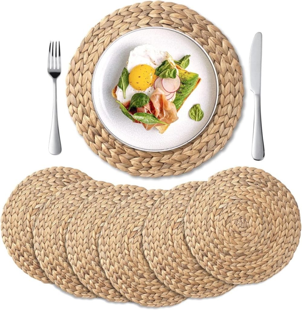 A set of six round woven placemats is shown, with one used under a plate of food, alongside a fork and knife—perfect for hosting friends like Theo of Golden Book Club.