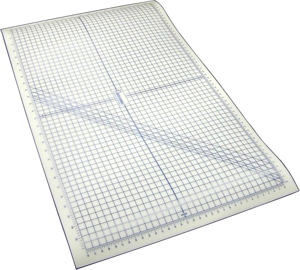 A large transparent gridded cutting mat with measurement markings along the edges and diagonal lines across the surface.
