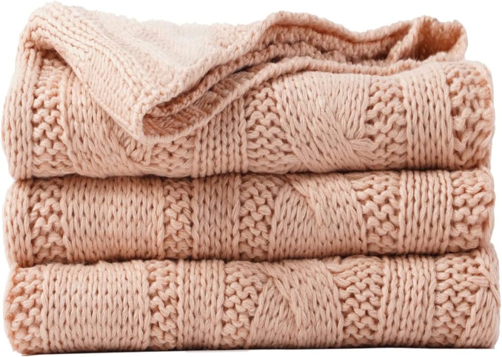 A folded, light peach-colored knitted blanket with a textured pattern.